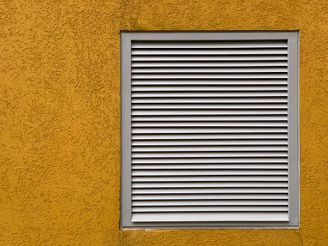 Square ventilation grate on a textured yellow wall