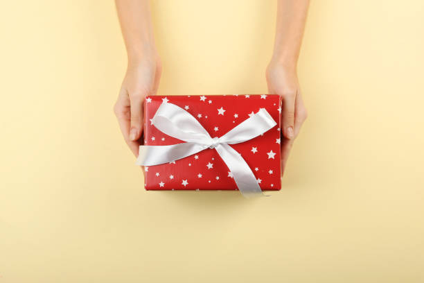 istock gift in female hands on a colored background top view. 1283691112