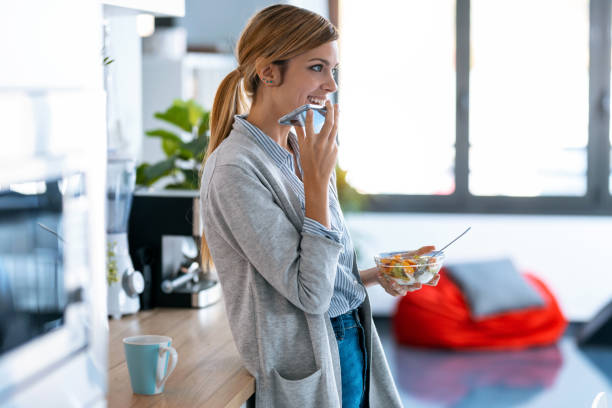 bella giovane donna che invia audio con cellulare mentre fa colazione sana in cucina a casa. - domestic staff audio foto e immagini stock