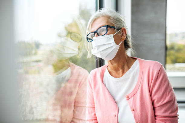 istock Senior adult in isolation looking through window with protective mask 1283693187