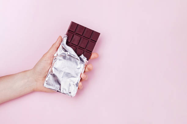 istock Hand holds dark chocolate bar in foil. 1283695103