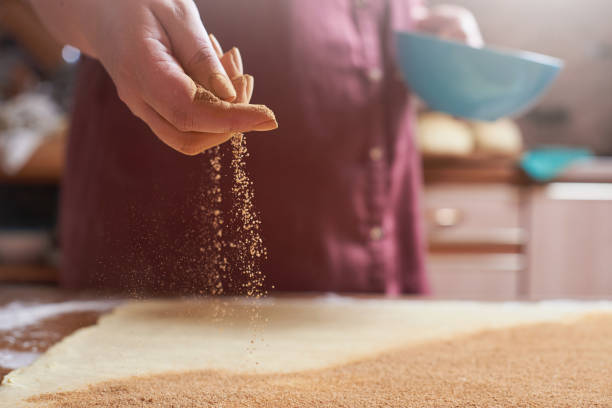 Female hand sprinkles cinnamon on a rolled raw dough for cinnamon buns stock photo