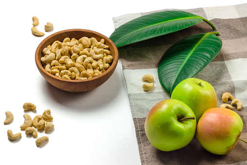 Cashew nuts in a wooden bowl, green leaves and apples isolated on white background top view. Clipping path stil photo