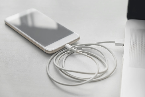 Close-up shot of a smartphone connected to a laptop for charge sharing, via a connected cable through USB port