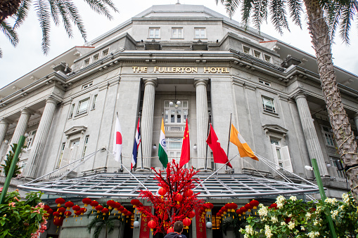 Singapore, 21/01/19. The Fullerton Hotel Singapore building front view of facade with Chinese New Year decorations, classical columns and flags.