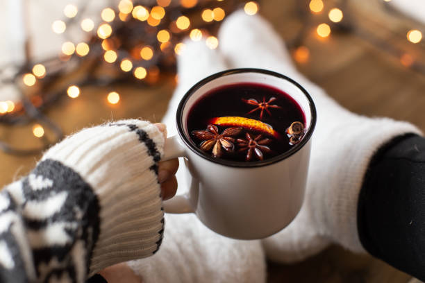 Mulled wine with spices Composition with a mug of hot red wine mulled wine with spices. Cozy holiday atmosphere, plush socks, warm sweater, Christmas lights on a dark background. mulled wine stock pictures, royalty-free photos & images