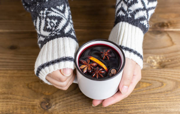 A mug of hot red mulled wine in woman hands Composition with a mug of hot red mulled wine with spices in woman hands. Cozy holiday atmosphere, warm sweater, Christmas atmosphere mulled wine photos stock pictures, royalty-free photos & images