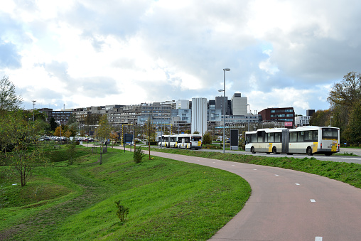 Leuven, Vlaams-Brabant, Belgium - November, 03, 2020: Gasthuisberg UZ-Leuven. Articulated busses going direction hospital. Pink asphalt, curved Bicycle lane path .