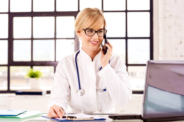 istock Smiling female doctor using phone and talking with her patient while sitting in doctor's office 1283710621