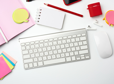 white wireless keyboard, computer mouse and paper notebook on white desktop, top view. Workplace