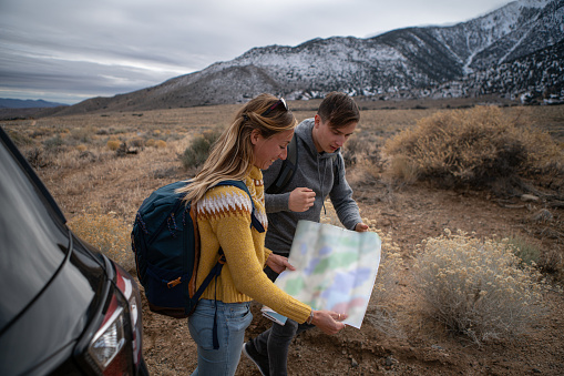 Young couple exploring USA and looking for directions on a map.\nShot in California with the Sierra Nevada mountains on background