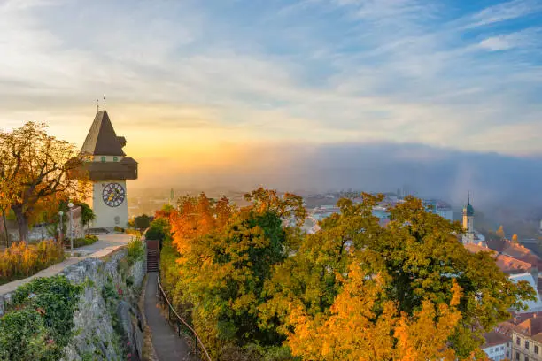 The famous clock tower on Schlossberg hill, in Graz, Styria region, Austria, at sunrise. Beautiful foggy morning over the city of Graz, in autumn