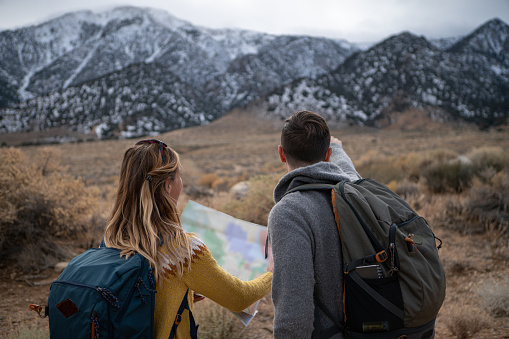 Young couple exploring USA and looking for directions on a map.\nShot in California with the Sierra Nevada mountains on background