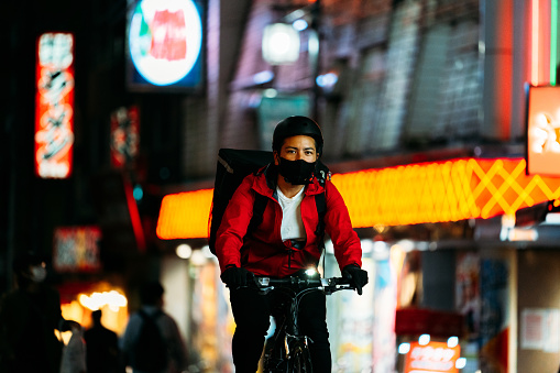 A food delivery person is cycling at night in the city.
