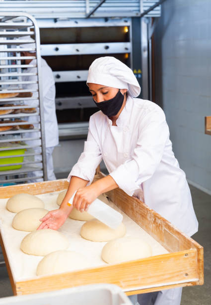 istock Professional baker wearing protective mask prepares raw loaves for baking in oven 1283714003