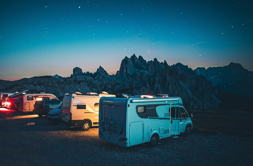 Row of Camper Vans Motorhomes on the Ridge at Night. Mountain RV Camping in the Italian Dolomites. Starry Summer Sky.