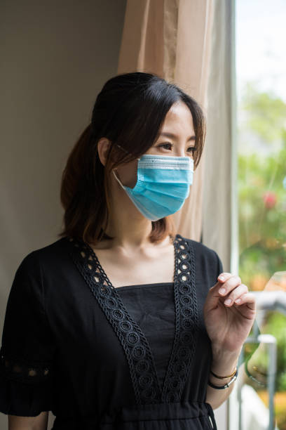 istock Young Asian woman with protective face mask looking through her balcony window during the restricted movement order. Quarantine and Self isolation at home during Covid-19 pandemic. 1283715584