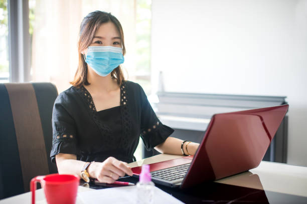 世界的なパンデミックの流行に対するmco(運動制御秩序)の間に保護フェイスマスクを着用し、自宅で働いているアジアの女性。 - m&co ストックフォトと画像