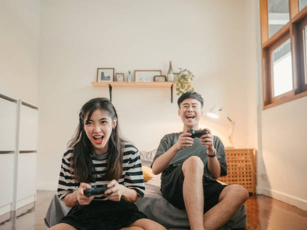 азиатская семья играет в видеоигры дома. - video game friendship teenager togetherness стоковые фото и изображения