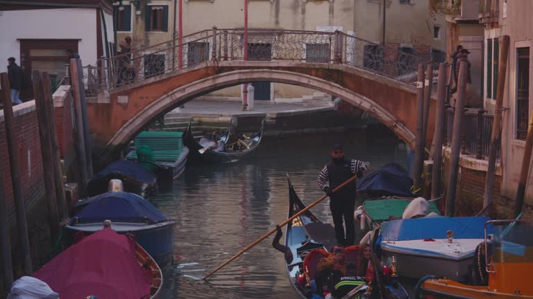 A gondolier steers a traditional gondola under a bridge in old Venice, Italy