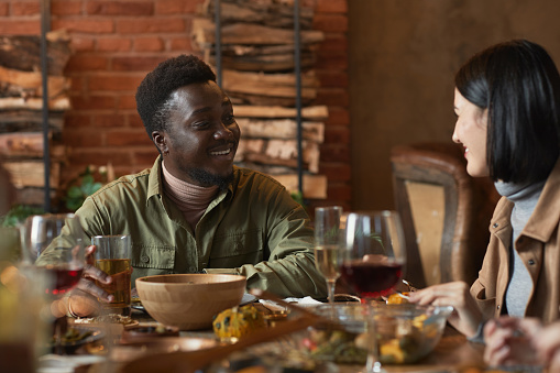 Portrait of young African-American man smiling at female friend while enjoying dinner party outdoors