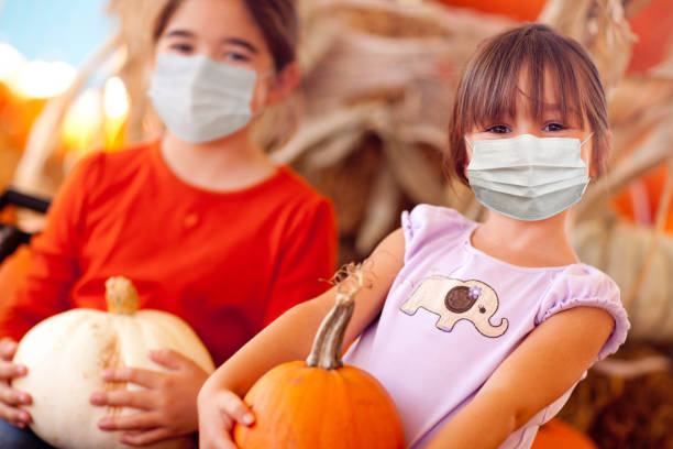 医療フェイスマスクを着用したカボチャのパッチでカボチャを保持しているかわいい女の子 - pumpkin child little girls pumpkin patch ストックフォトと画像