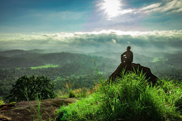 luz de fondo del hombre viendo la increíble vista de las capas de montaña cubiertas de niebla blanca al amanecer - wayanad fotografías e imágenes de stock