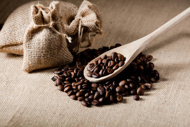 istock Coffee beans, on wooden spoon, with raffia cloth bag, light brown background 1283720223