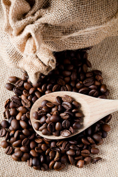 istock Coffee beans, on wooden spoon, with raffia cloth bag, light brown background 1283720304