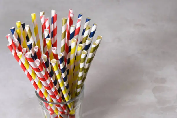 A glass filled with multi colored eco-friendly paper drinking straws. Horizontal format gray background with copy space.