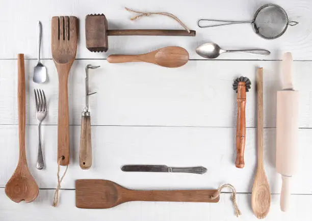 Top view of a group of cooking utensils on a rustic wood kitchen table arranged around a blank space for your copy.