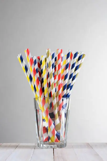 A bunch of multi-colored drinking straws .The straws are fanned out in a drinking glass on a wood table against a light to dark gray background.