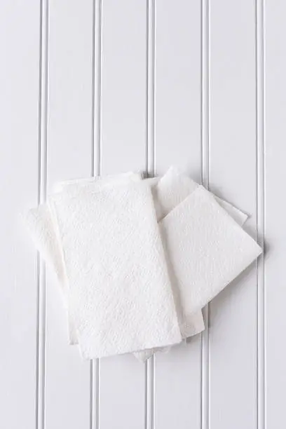 High angle view of a pile of white paper napkins on a white picnic table. Vertical format with copy space.