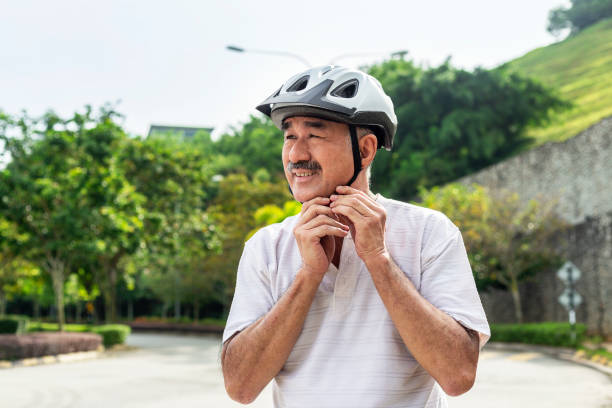 Senior Asian Man Adjusting Cycling Helmet In the City street senior male cyclist of Chinese descent at the park, getting ready to ride his bicycle. He is buckling his bike helmet. man 60s bicycle stock pictures, royalty-free photos & images