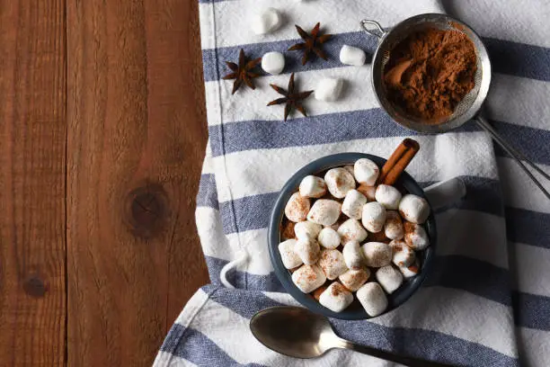 A mug of hot cocoa on a kitchen towel and rustic wood table with copy space.