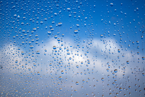 Rain drops on a window. Natural abstract pattern. Blue sky background. Selective focus.