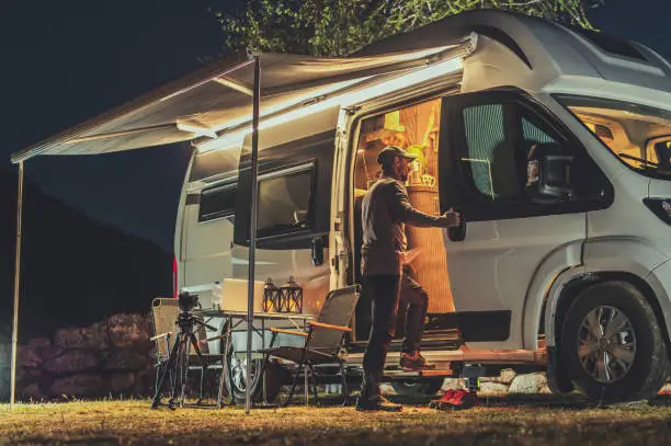 Caucasian Men and His Camper Van During Late Evening Hours. Motorhome RV Park Camping. Travel and Recreational Vehicles Theme.