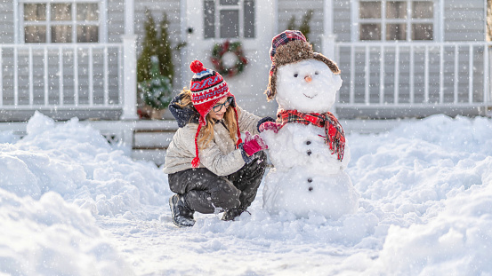Girl playing with a snowman in front of the house