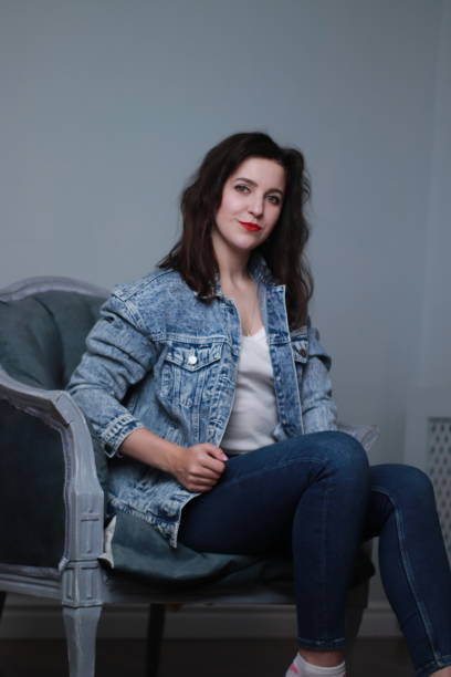 istock attractive brunette in jeans and denim jacket sitting on grey chair. studio shoot 1283729993