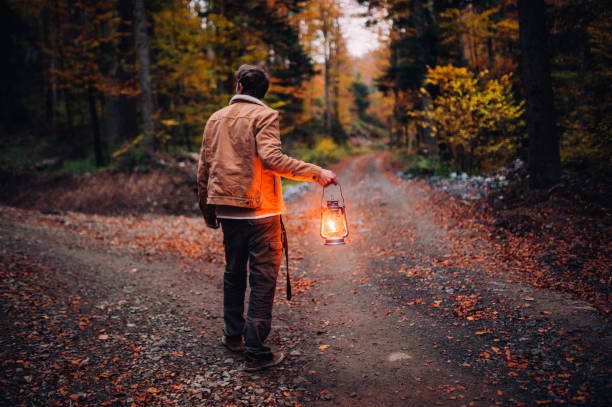 un homme avec une lanterne à un carrefour dans les bois - lanterne photos et images de collection