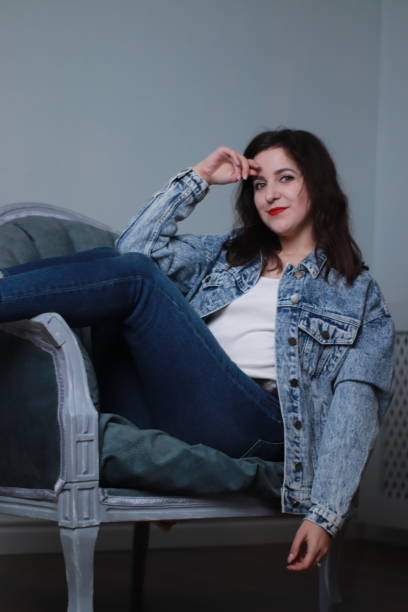 istock attractive brunette in jeans and denim jacket sitting on grey chair. studio shoot 1283730109