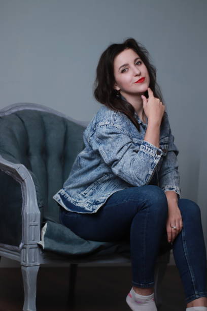 istock attractive brunette in jeans and denim jacket sitting on grey chair. studio shoot 1283730623