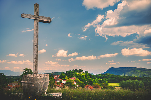 Wooden cross overlooking the small french village of Innimond in Bugey mountains, in Ain, Auvergne-Rhone-Alpes region in France European Alps during a sunny spring day.