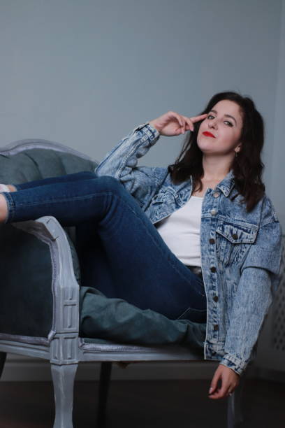 istock attractive brunette in jeans and denim jacket sitting on grey chair. studio shoot 1283731495