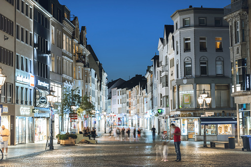 view from Bonn market square to illuminated shopping street at blue hour of late summer evening, few people on the streets