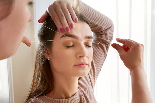 Cosmetologist plucks client eyebrows by thread in the beauty salon The make-up artist plucks eyebrows with a thread close-up. Face care beauty treatments in the beauty salon hair threading stock pictures, royalty-free photos & images