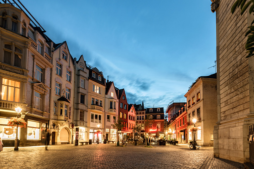 small illuminated town square in the historic center of Aachen at blue hour with street restaurant, only few people in the background
