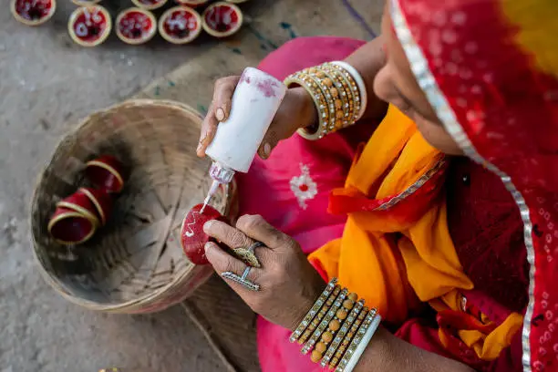 Photo of Indian woman in traditional costume and bangles decorating and painting a small clay bowl