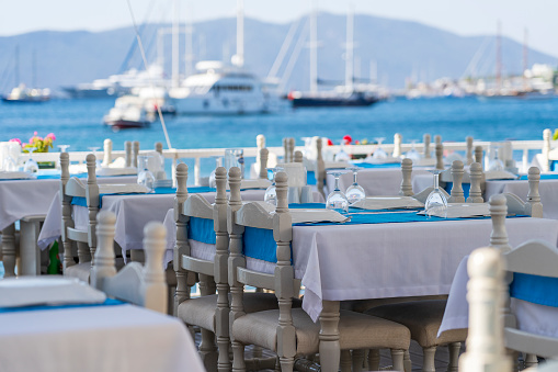 Elegant table setting with fork, knife, wine glass, white plate and blue napkin in restaurant. Nice dining table set with arranged silverware and napkin for dinner, Bodrum, Turkey. Beach cafe near sea