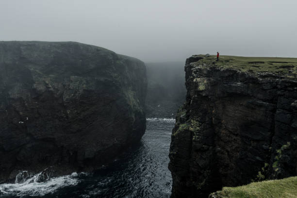 Lonely tourist on a hike along the cliffs of Eshaness, cold autumn day, Shetland Islands.